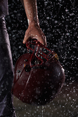 Image showing Close up of American Football Athlete Warrior Standing on a Field focus on his Helmet and Ready to Play. Player Preparing to Run, Attack and Score Touchdown. Rainy Night with Dramatic lens flare