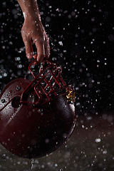 Image showing Close up of American Football Athlete Warrior Standing on a Field focus on his Helmet and Ready to Play. Player Preparing to Run, Attack and Score Touchdown. Rainy Night with Dramatic lens flare