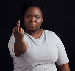 Image showing Portrait, anger and black woman with middle finger, opinion and angry expression on a dark studio background. Face, female person and African model with hate sign, rude and frustrated with conflict