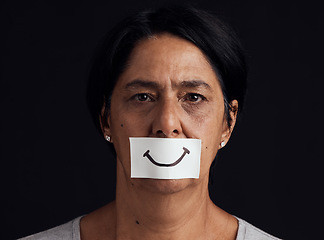 Image showing Portrait, fake smile or abuse and a mature woman in studio on a dark background with an expression. Depression, anxiety and mental health with a female person looking brave to hide her emotions