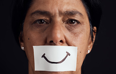 Image showing Portrait, smile or anxiety and a mature woman in studio on a dark background with a fake expression. Depression, abuse and mental health with a female person looking brave to hide her emotions