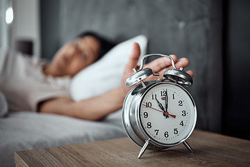 Image showing Alarm, sleeping and a hand with a clock for awake, oversleep or tired in the bedroom of a home. House, ring and a closeup of a person or woman in bed for snooze, rest or waking up lazy in a house