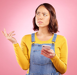 Image showing Thinking, studio and Asian woman with cellphone problem, bad news and stress over mistake, crisis or social media post. Frustrated, doubt and person confused over smartphone glitch on pink background