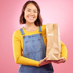 Image showing Woman, paper bag and studio portrait with shopping, discount or groceries with smile by pink background. Japanese gen z girl, retail customer and package for product, sale and excited for cheap deal