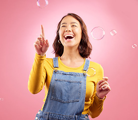 Image showing Happy, woman and laughing with bubbles in studio, pink background and excited to celebrate freedom, play and creativity. Asian female model pop soap bubble for funny, entertainment and burst of magic