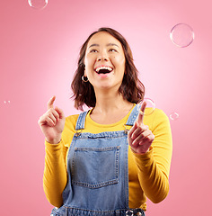 Image showing Happy, woman and play with bubbles in studio, pink background and excited to celebrate freedom. Asian female model pop liquid soap bubble for fun, entertainment and burst of magic, color and creative