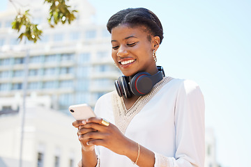 Image showing Phone, city and music with a business black woman typing a text message while walking to work outdoor. Mobile, headphones and social media with a happy employee commuting in an urban town with flare