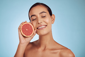 Image showing Happy woman, grapefruit and vitamin C for skincare or diet against a blue studio background. Face of female person with organic citrus fruit for natural nutrition, dermatology or healthy wellness