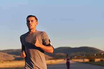 Image showing A handsome young couple running together during the early morning hours, with the mesmerizing sunrise casting a warm glow, symbolizing their shared love and vitality