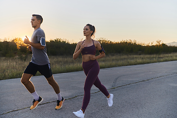 Image showing A handsome young couple running together during the early morning hours, with the mesmerizing sunrise casting a warm glow, symbolizing their shared love and vitality