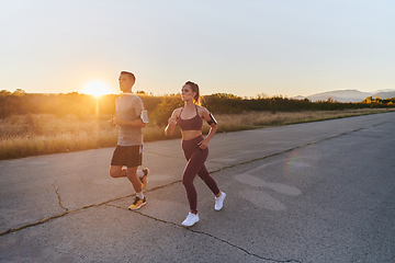 Image showing A handsome young couple running together during the early morning hours, with the mesmerizing sunrise casting a warm glow, symbolizing their shared love and vitality