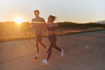 Image showing A handsome young couple running together during the early morning hours, with the mesmerizing sunrise casting a warm glow, symbolizing their shared love and vitality