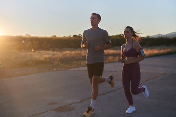 Image showing A handsome young couple running together during the early morning hours, with the mesmerizing sunrise casting a warm glow, symbolizing their shared love and vitality