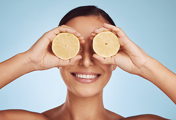Image showing Happy woman, hands and lemon eyes for skincare detox, diet or collagen against a blue studio background. Female person with organic citrus fruit for natural nutrition, anti aging or facial treatment