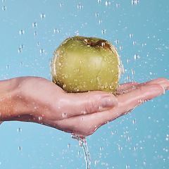 Image showing Health, water and a hand with an apple on a blue background for nutrition, cleaning or wellness. Diet, food and closeup of a person with a fruit in palm for a detox isolated on a studio backdrop