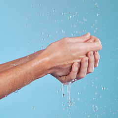 Image showing Water drops, hygiene and a person washing hands in studio on a blue background for cleaning or hydration. Beauty, wellness and skincare with a splash in the bathroom for sustainability or health