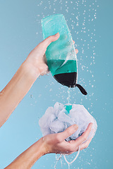 Image showing Woman, hands and loofah with soap in shower for hygiene, washing or cleaning body against a blue studio background. Closeup of female person pouring gel bottle with falling water or rain on sponge