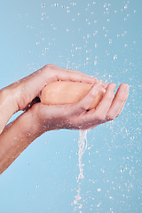 Image showing Water, soap and a person washing hands in studio on a blue background for hygiene or hydration. Cleaning, wellness and skincare with an adult in the bathroom to remove bacteria or germs for health