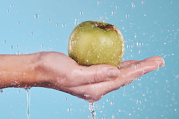 Image showing Vegan, water and a hand with an apple on a blue background for nutrition, cleaning or wellness. Diet, food and closeup of a person with a fruit in palm for a detox isolated on a studio backdrop