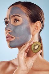 Image showing Thinking, kiwi and mask for beauty with a woman in studio on a blue background for antiaging skincare. Face, facial and fruit with a young female model holding a berry for natural organic treatment