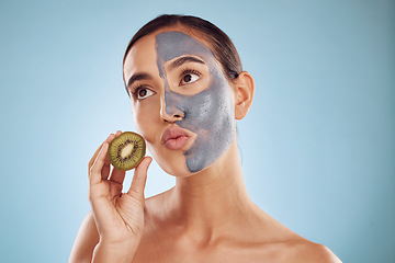 Image showing Thinking, kiwi and mask for skincare with a woman in studio on a blue background for antiaging treatment. Face, facial and pout with an attractive young female holding a berry for natural beauty