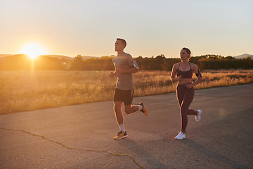 Image showing A handsome young couple running together during the early morning hours, with the mesmerizing sunrise casting a warm glow, symbolizing their shared love and vitality