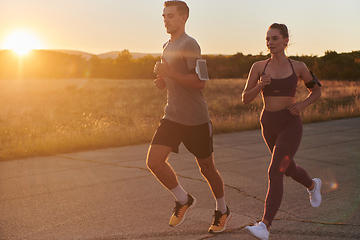 Image showing A handsome young couple running together during the early morning hours, with the mesmerizing sunrise casting a warm glow, symbolizing their shared love and vitality