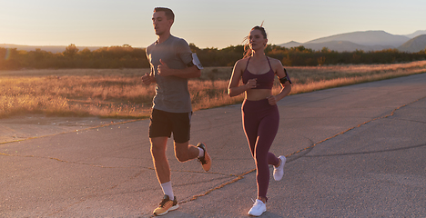 Image showing A handsome young couple running together during the early morning hours, with the mesmerizing sunrise casting a warm glow, symbolizing their shared love and vitality