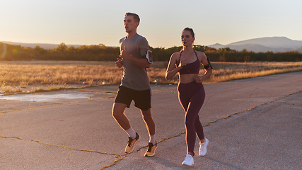 Image showing A handsome young couple running together during the early morning hours, with the mesmerizing sunrise casting a warm glow, symbolizing their shared love and vitality