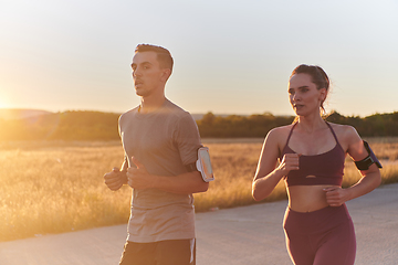 Image showing A handsome young couple running together during the early morning hours, with the mesmerizing sunrise casting a warm glow, symbolizing their shared love and vitality