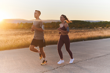 Image showing A handsome young couple running together during the early morning hours, with the mesmerizing sunrise casting a warm glow, symbolizing their shared love and vitality