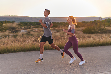 Image showing A handsome young couple running together during the early morning hours, with the mesmerizing sunrise casting a warm glow, symbolizing their shared love and vitality