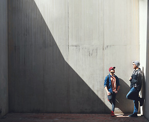 Image showing Fashion, friends and men in a city talking, bond and hanging out on the weekend against wall background. Chilling, conversation and male people downtown for fun, freedom and off day with trendy style