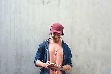 Image showing Happy, music and a man with a phone on a wall for social media, communication or a chat. Smile, technology and a male college student streaming or listening to a podcast on a mobile app with space