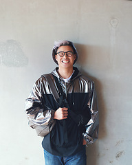 Image showing Portrait, fashion and Asian man with a smile, streetwear and stylish outfit against a wall background. Male person, happy model and student with glasses, trendy clothes and happiness with confidence