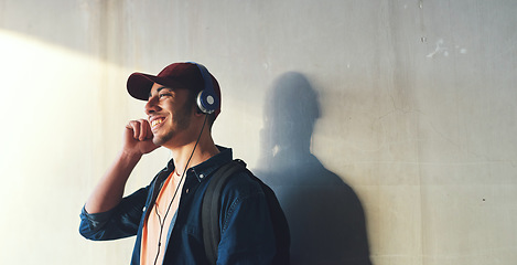 Image showing Happy man, student and headphones, listening to music on campus with happiness and audio against wall background. Gen z, education and male person at college, mockup space and podcast streaming