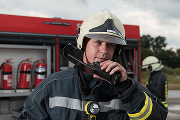 Image showing fireman using walkie talkie at rescue action fire truck and fireman's team in background.