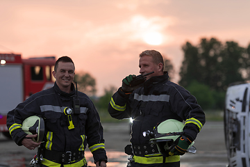 Image showing fireman using walkie talkie at rescue action fire truck and fireman's team in background.