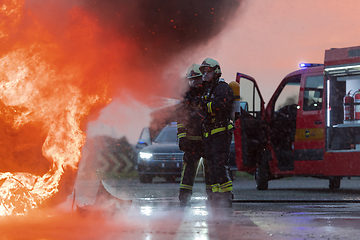Image showing Firefighters using water fire extinguisher to fighting with the fire flame in car accident. Firefighter industrial and public safety concept rescue in night.