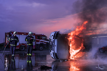 Image showing Firefighters using water fire extinguisher to fighting with the fire flame in car accident. Firefighter industrial and public safety concept rescue in night.