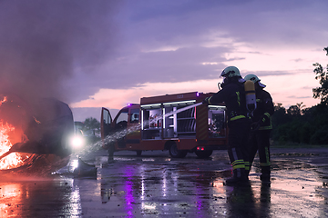 Image showing Firefighters using water fire extinguisher to fighting with the fire flame in car accident. Firefighter industrial and public safety concept rescue in night.