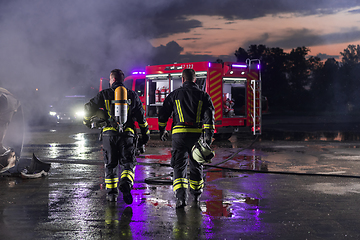 Image showing Brave Firefighters Team Walking to the Camera. In Background Paramedics and Firemen Rescue Team Fight Fire in Car Accident, Insurance and Save Peoples Lives concept.