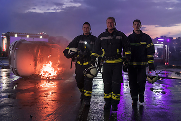 Image showing Brave Firefighters Team Walking to the Camera. In Background Paramedics and Firemen Rescue Team Fight Fire in Car Accident, Insurance and Save Peoples Lives concept.