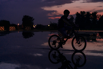 Image showing Lonely children silhouette on bike, boy riding bicycle on reflective water. Background beautiful sunset.