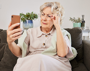 Image showing Cellphone, glasses and elderly woman reading a text message, blog or online news on sofa in the living room. Vision, technology and senior female person squinting while networking on a phone at home.