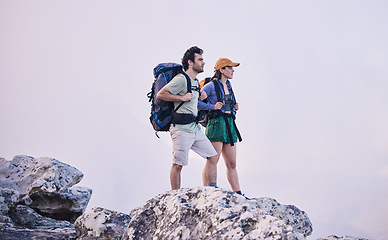 Image showing Mountains, hiking and man with woman on cliff for adventure in nature, landscape and travel. Outdoor trekking, couple on peak and relax in scenic clouds for natural journey, walking and rock climbing