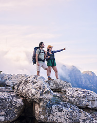 Image showing Mountains, hiking and pointing, man and woman on peak for adventure in nature, landscape and travel. Outdoor trekking, couple on cliff and relax in scenic clouds for natural journey, view and looking