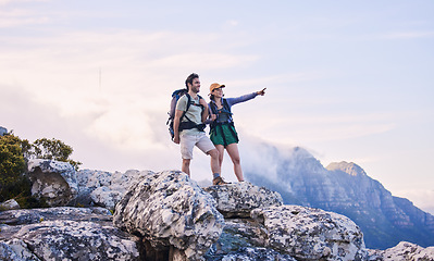 Image showing Mountain, trekking and view, man with woman on peak for adventure in nature, rock climbing and travel. Outdoor hiking, couple on cliff and relax in scenic clouds for natural journey, pointing at sky.