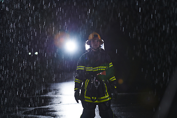 Image showing A determined female firefighter in a professional uniform striding through the dangerous, rainy night on a daring rescue mission, showcasing her unwavering bravery and commitment to saving lives.