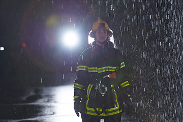 Image showing A determined female firefighter in a professional uniform striding through the dangerous, rainy night on a daring rescue mission, showcasing her unwavering bravery and commitment to saving lives.